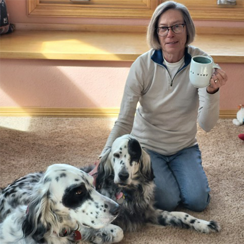 a woman holding a be kind ceramic mug with her two dogs 