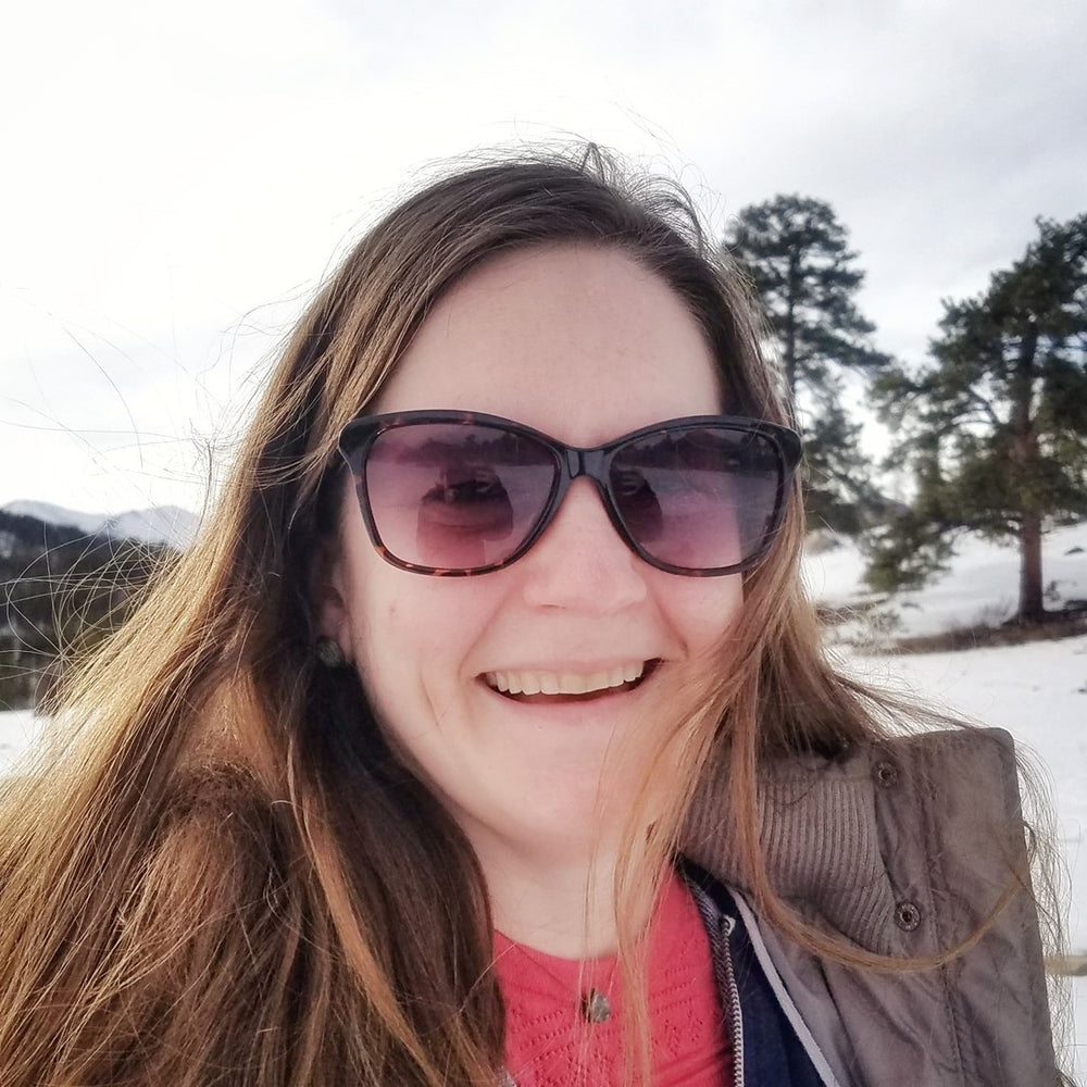 woman in sunglasses smiling outside with snow in the background 