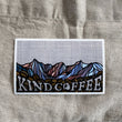 Load image into Gallery viewer, Mountain Sticker with a colorful mountain background, espresso beans, and "Kind Coffee" in the foreground