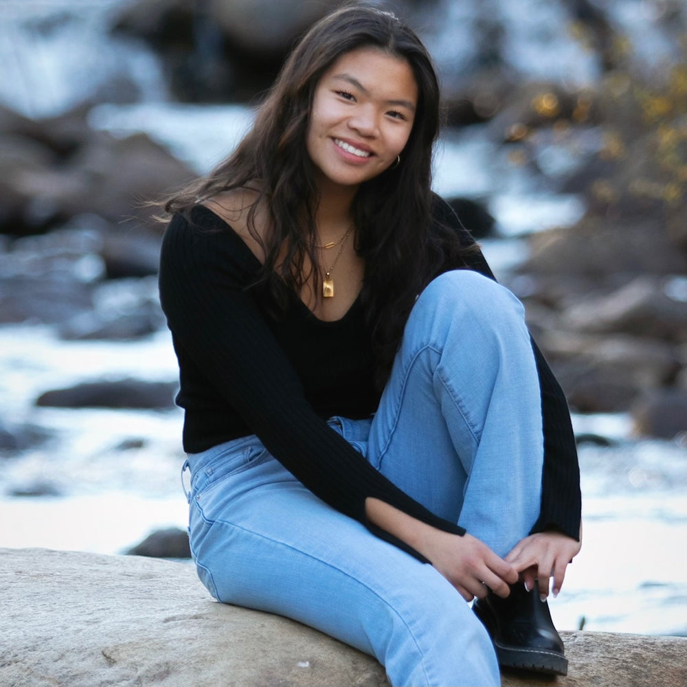 smiling girl in black shirt sitting on a rock riverside