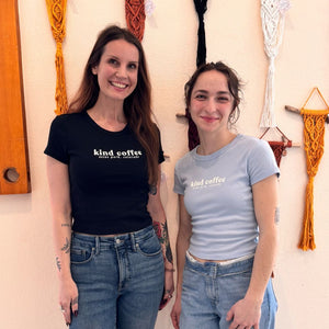 two women posing in a small t-shirt that says "kind coffee, estes park colorado" across the chest 