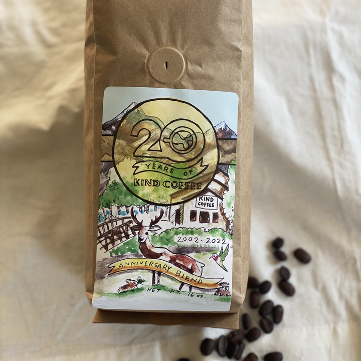 1 lb bag of 20th Anniversary coffee, whole bean. Sitting on a white cloth backdrop with coffee beans sprinkled at the bottom