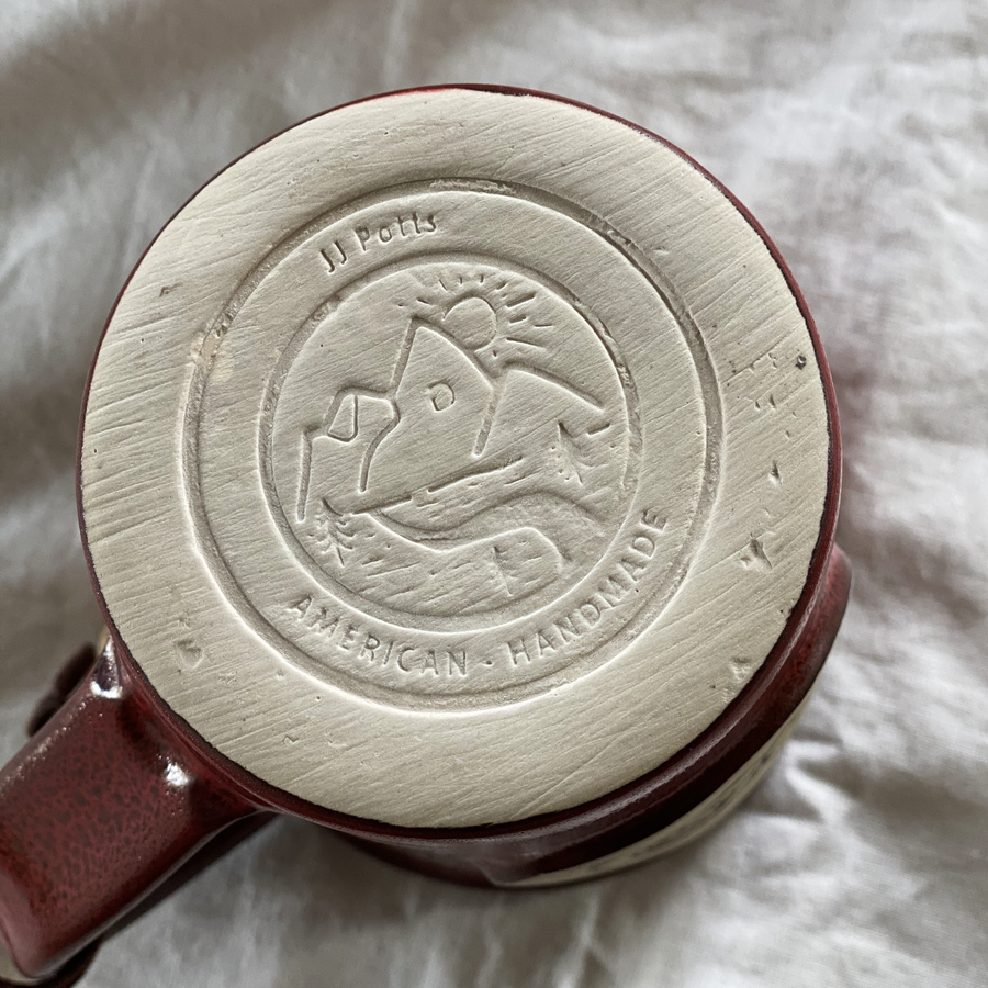 Un-glazed bottom of ceramic mug that reads "JJ Potts American - Handmade" with an etched mountain scene