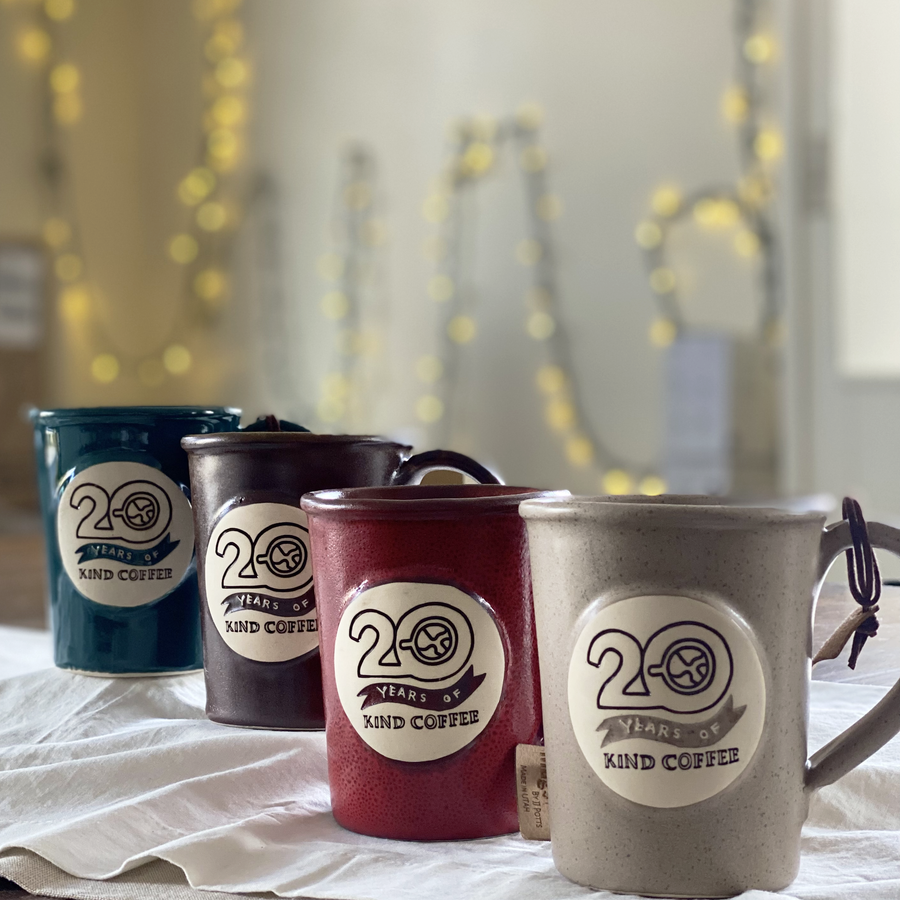 Four ceramic mugs that read "20 Years of Kind Coffee" in sandstone, red, brown, and dark teal