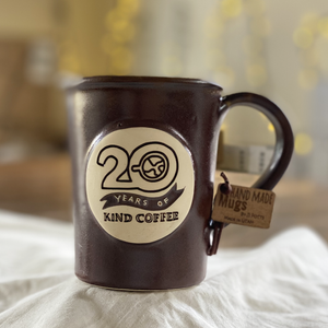 Brown ceramic mug with "20 Years of Kind Coffee" on a white cloth