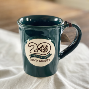 Dark teal ceramic mug with "20 Years of Kind Coffee" on a white cloth