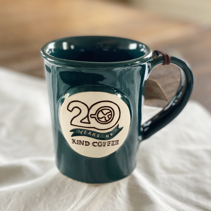 Dark teal ceramic mug with "20 Years of Kind Coffee" on a white cloth