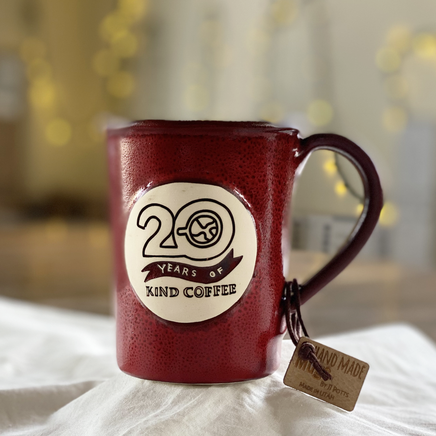 Brick Red ceramic mug with "20 Years of Kind Coffee" on a white cloth