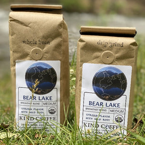 Two Bear Lake 1 lb bags of coffee, one whole bean and one drip grind, sitting in the grass. 